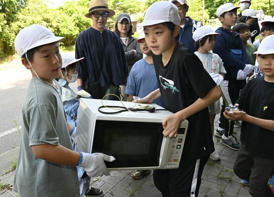 不法投棄された電子レンジを運ぶ児童ら