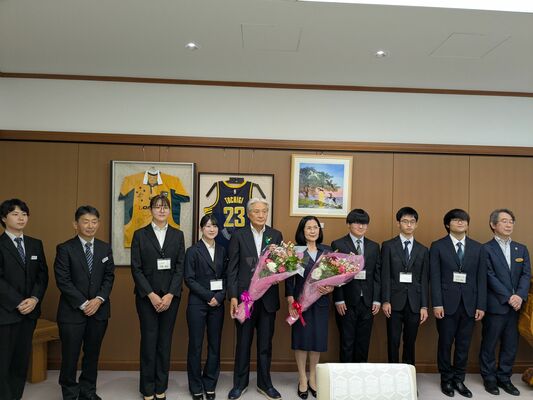 知事（左から５人目）と喜江子さん（同６人目）に花束を贈呈した学生ら＝７日午前、県庁