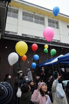 雪が降る中で一斉に風船を飛ばす安良沢小の児童ら