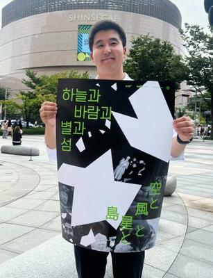 　映画「空と風と星と島」のポスターを手にする金明允さん＝１９日、韓国・釜山（共同）
