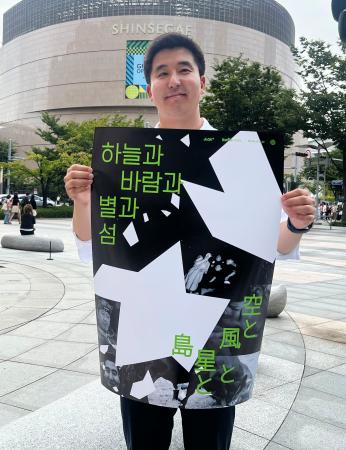 映画「空と風と星と島」のポスターを手にする金明允さん=19日、韓国・釜山(共同)