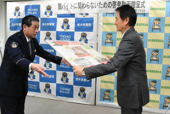 阿久澤教育長（右）にパネルを手渡す佐藤生活安全部長＝24日午後、県庁南別館