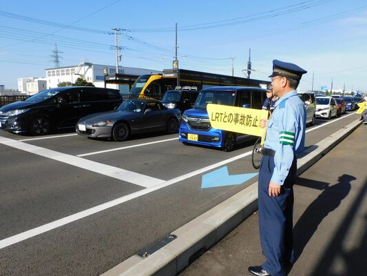 ハンドボードを掲げてＬＲＴとの交通事故防止を訴える生井真岡署長＝25日午前、芳賀町芳賀台（県警提供）