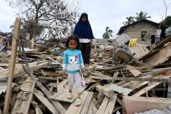 　がれきを通り、家から外出する親子＝２６日、インドネシア・クアラシンパン（共同）