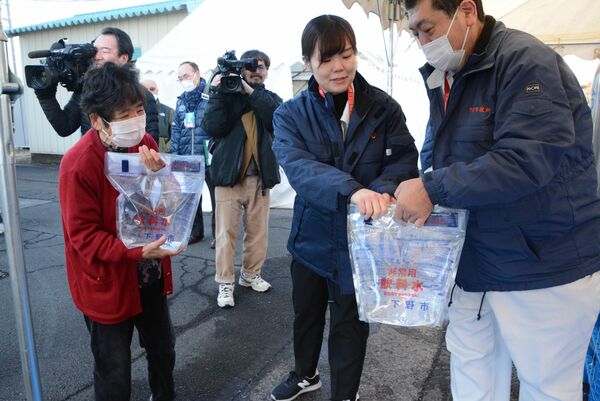 臨時給水所で、飲料水が入った給水袋を受け取る住民（手前左）ら＝４日午前９時、石橋北小