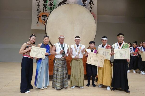 コンテスト終了後にトロフィーなどを手にする龍さん（中央）、光さん（左から３人目）、山崎さん（同２人目）と本選に出場した岩舟武蔵太鼓のメンバー（岩舟武蔵太鼓提供）