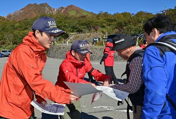 登山者（右）にチラシを配って安全な登山を呼びかける消防署員＝13日午前８時50分、那須町湯本
